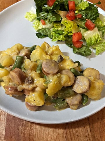 A plate with cheesy brat stew and a salad, ready to eat.