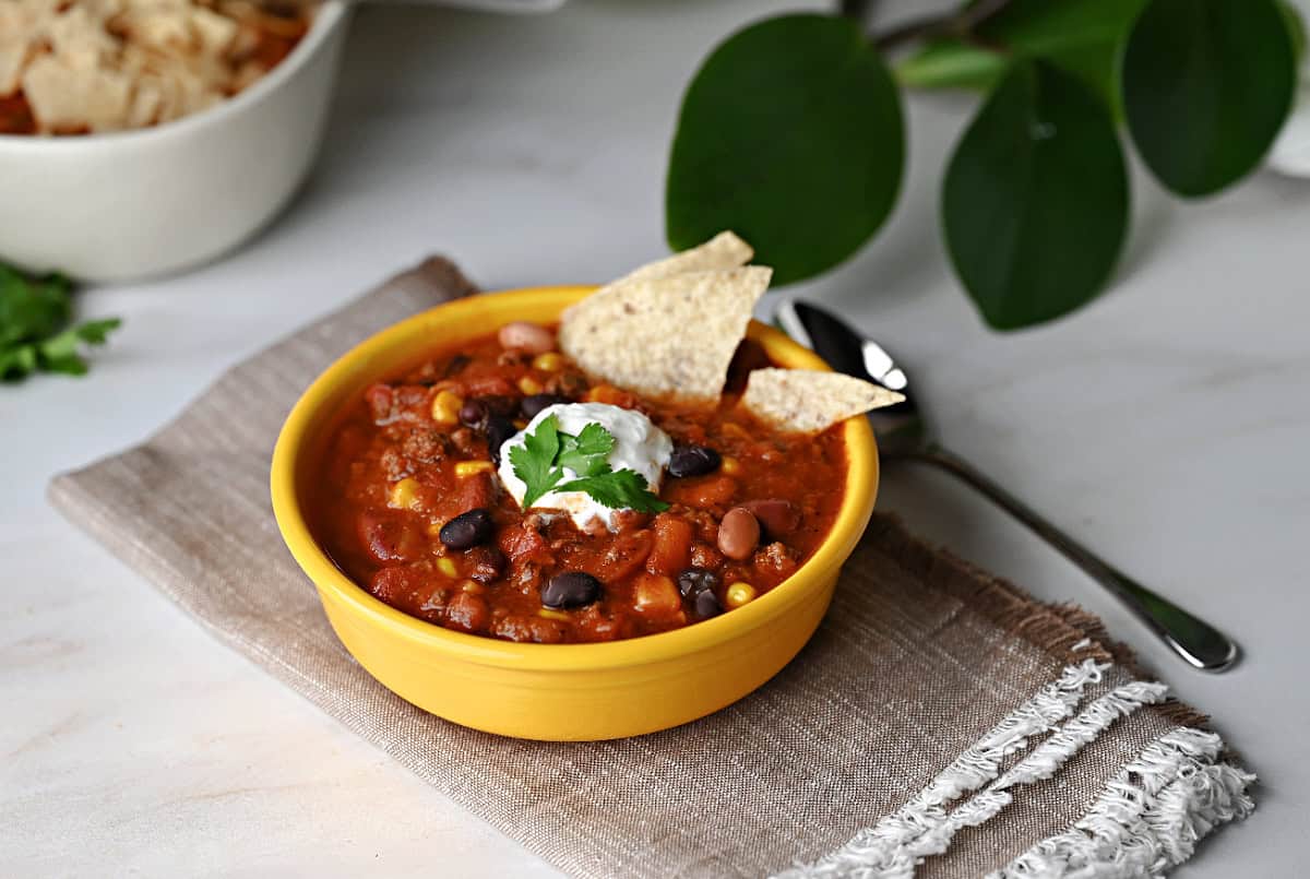 A bowl of taco chili garnished with sour cream and tortilla chips.