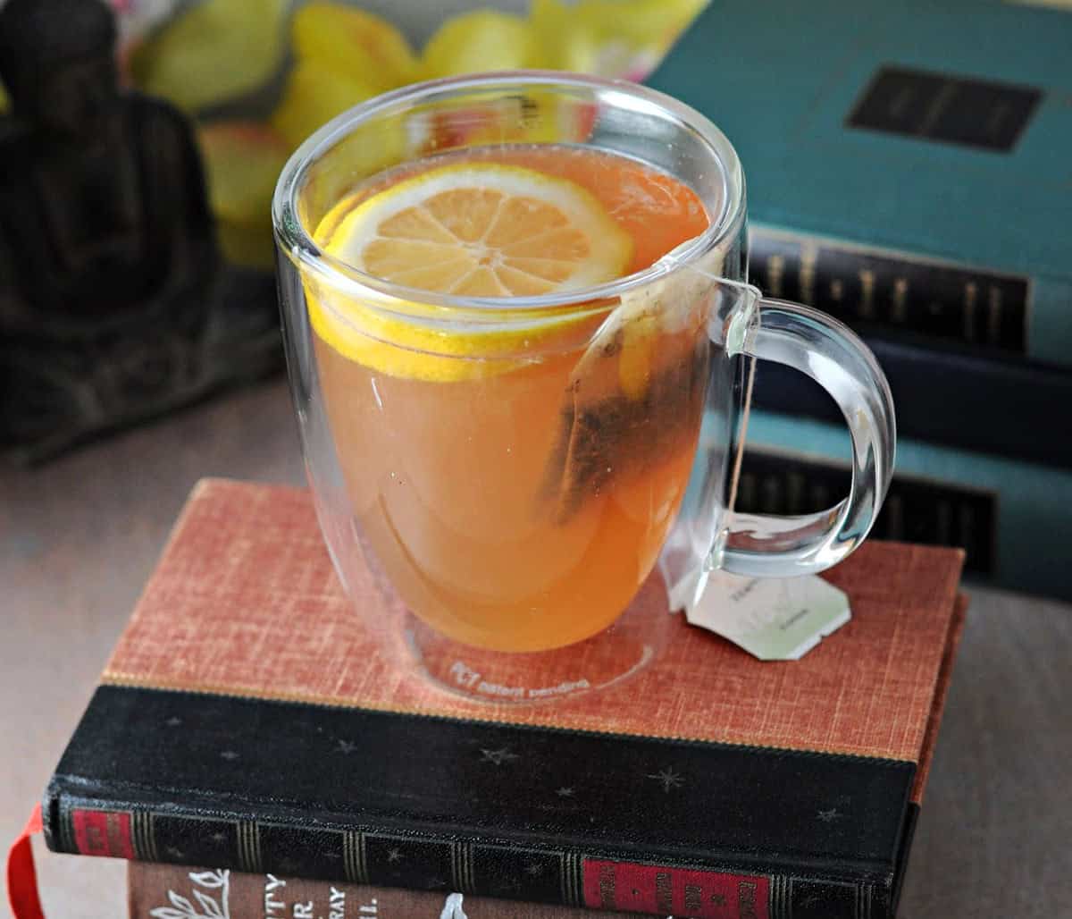 A clear mug of tea sitting on top of a stack of books.