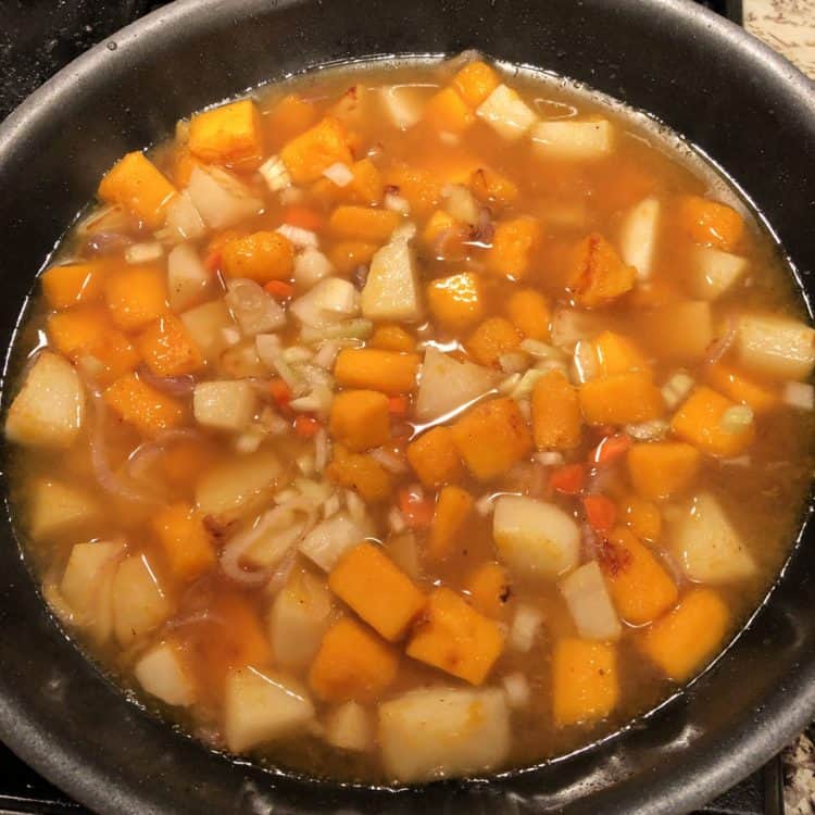Uncooked squash and potato cubes in a pot with broth