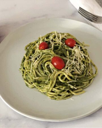 green pasta sauce on spaghetti noodles, on a white plate