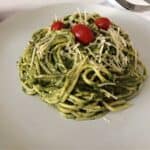 Green pasta sauce on spaghetti noodles, sitting on a white plate