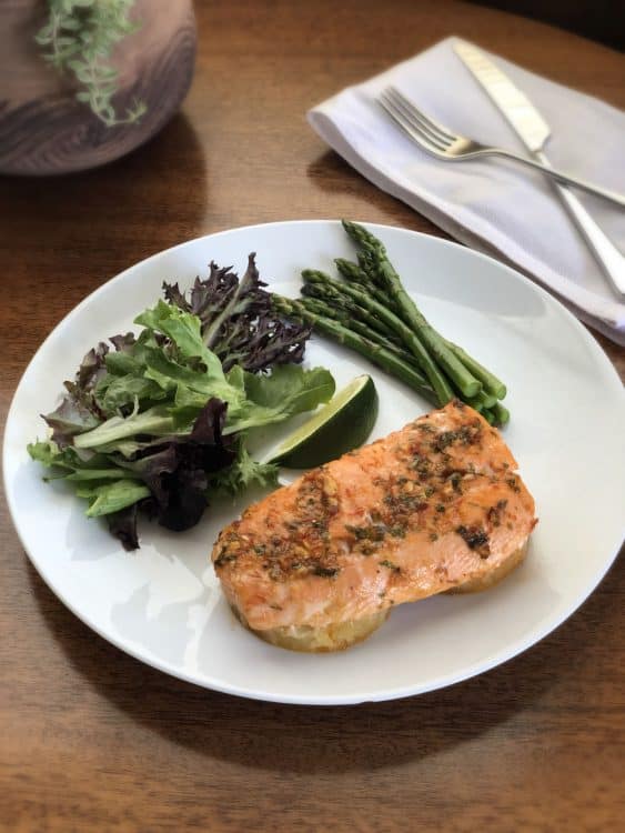 baked pineapple salmon on a white plate with salad and asparagus