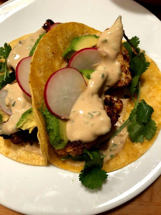 cauliflower tacos with extra sauce on a white plate