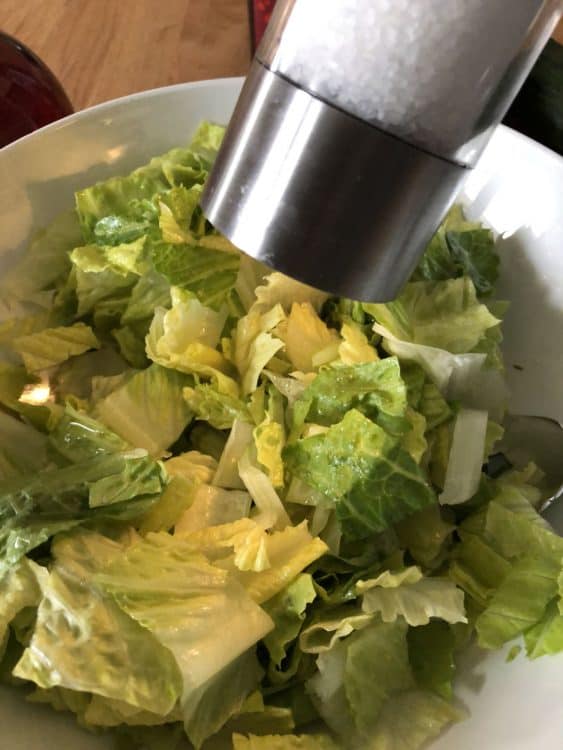 adding salt to the lettuce in the bowl