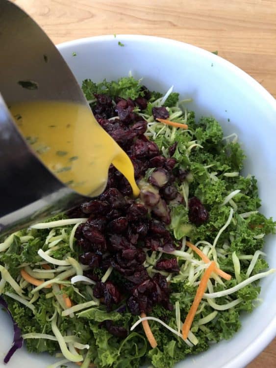 pouring dressing into the bowl of broccoli kale salad