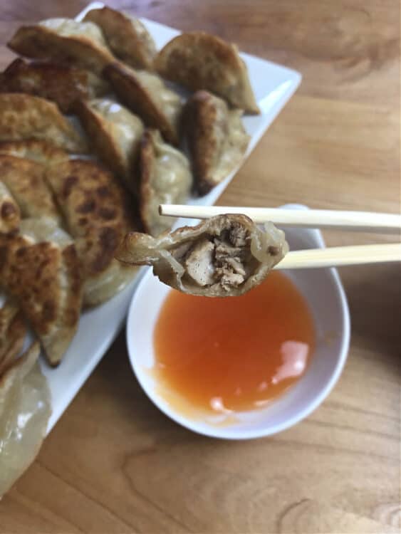 chopsticks holding one chinese dumpling with a bite taken, showing the filling inside