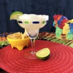 margarita slush in a stemmed glass on a red placemat with chips and a lime