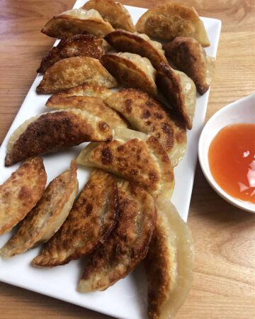 serving platter of potstickers with some dipping sauce