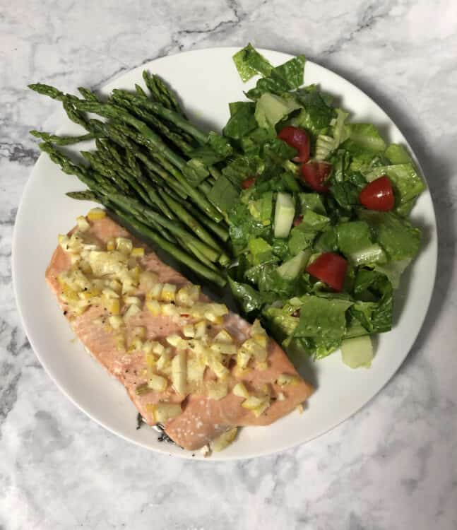 top down of salmon with lemon dressing on a plate with salad and asparagus