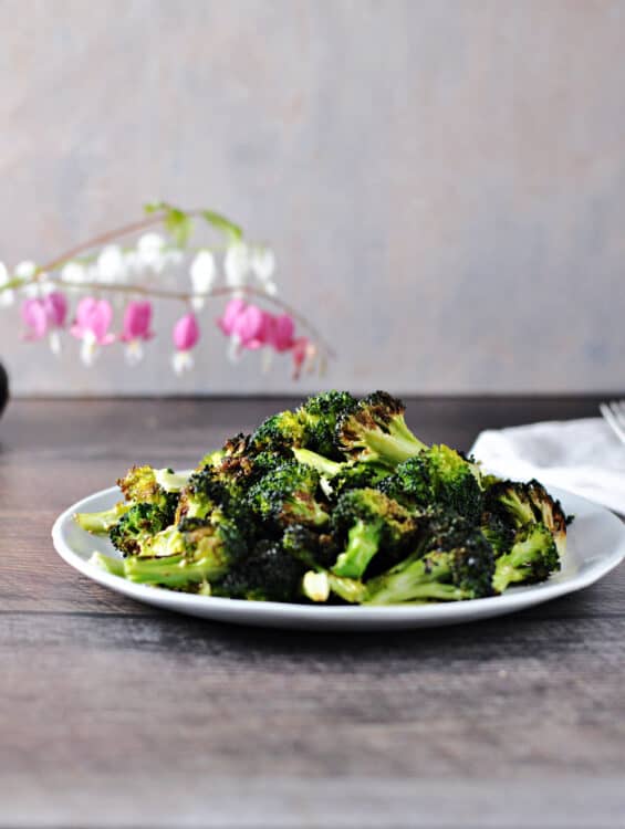 Air fryer broccoli on a small white plate with pink and white flowers in the background