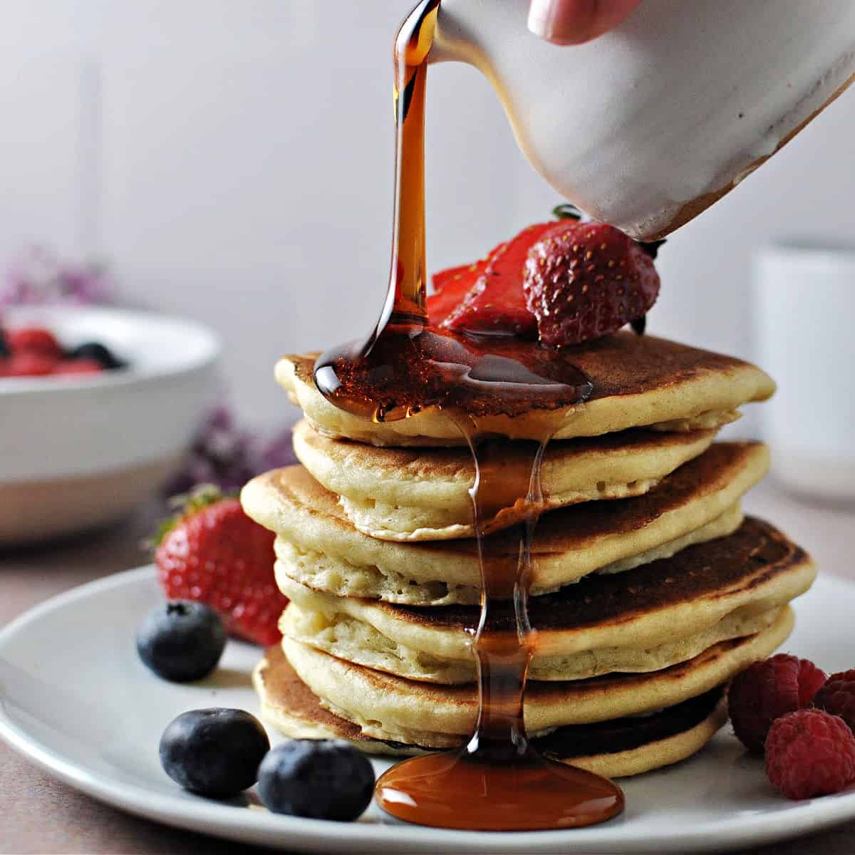 stack of almond milk pancakes with fruit and syrup being poured over