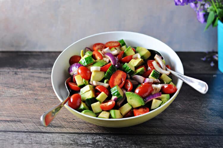 ba;samic cucumber tomato salad in a serving bowl with 2 serving spoons