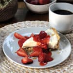 no bake cheesecake slice on a plate with strawberry sauce on top and a cup of coffee nearby