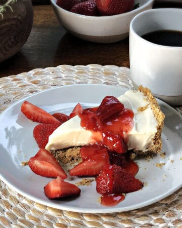 no bake cheesecake slice on a plate with strawberry sauce on top and a cup of coffee nearby