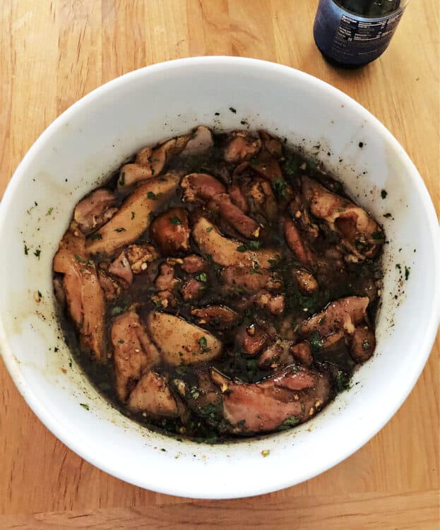 cut up chicken pieces soaking in marinade in a white bowl