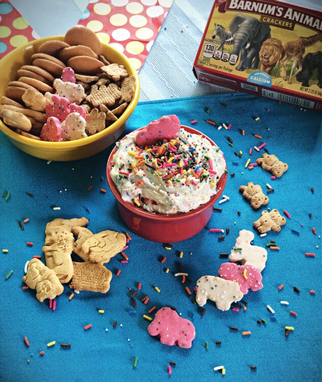 bowl of dip garnished with sprinkles and surrounded by cookies and crackers for dipping