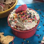 Dunkaroo Dip, also known as funfetti cake batter dip, in a small bowl garnished with sprinkles and surrounded by crackers and cookies for dipping