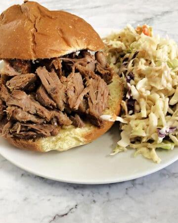 pulled pork on a sandwich bun with coleslaw on a white plate