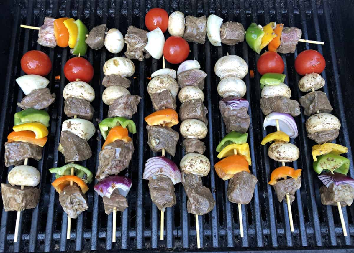 Beef steak kabobs cooking on a grill.