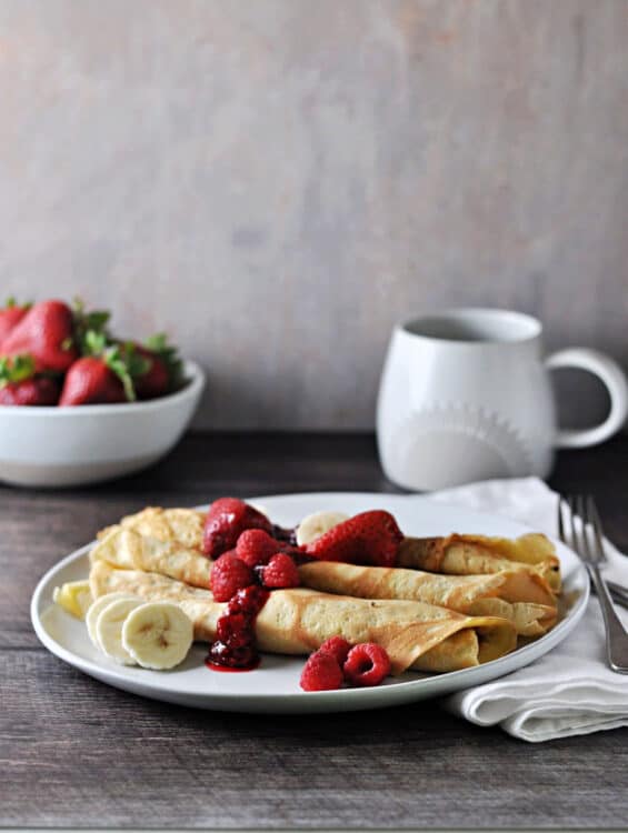 3 crepes on a plate with fruit and berry sauce