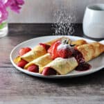 almond milk crepes with fruit being dusted with powdered sugar