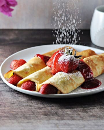 almond milk crepes with fruit being dusted with powdered sugar