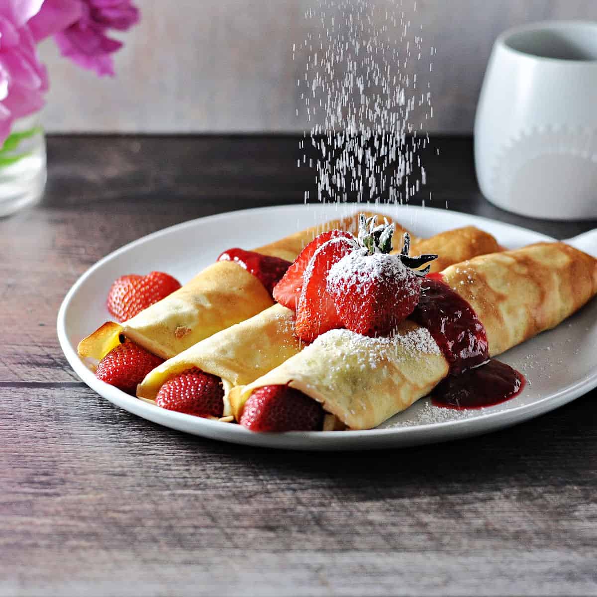 almond milk crepes with fruit, getting dusted with powdered sugar