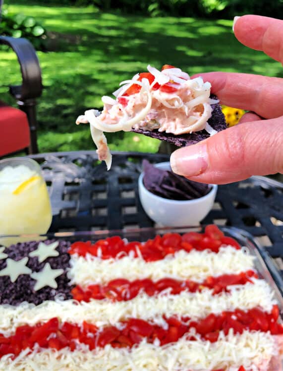 hand holding a chip covered in dip with whole pan of taco dip behind and outdoors