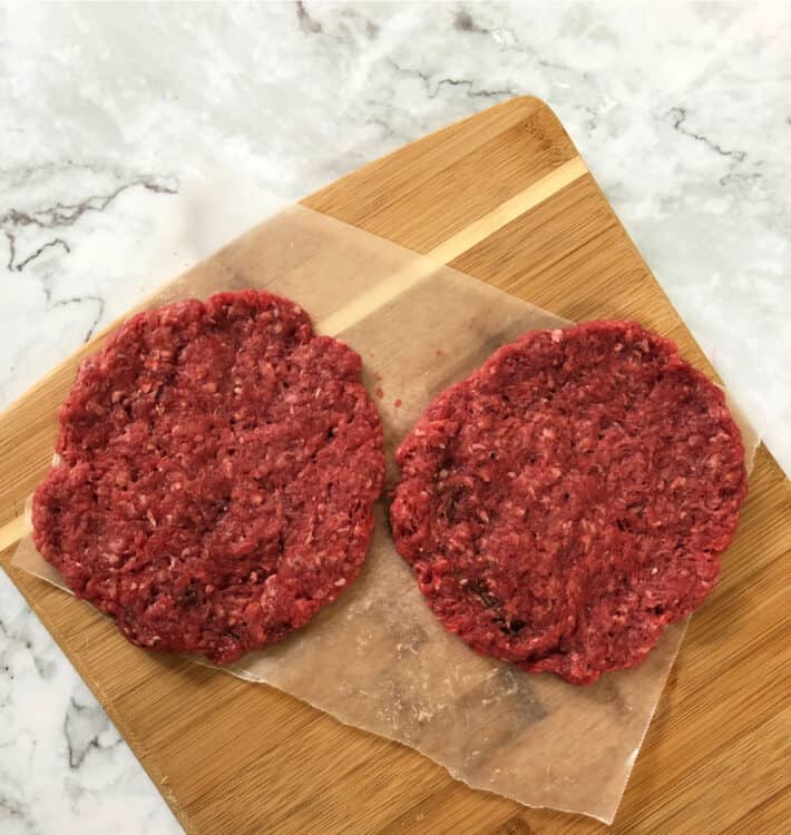 2 burger patties on a bamboo cutting board