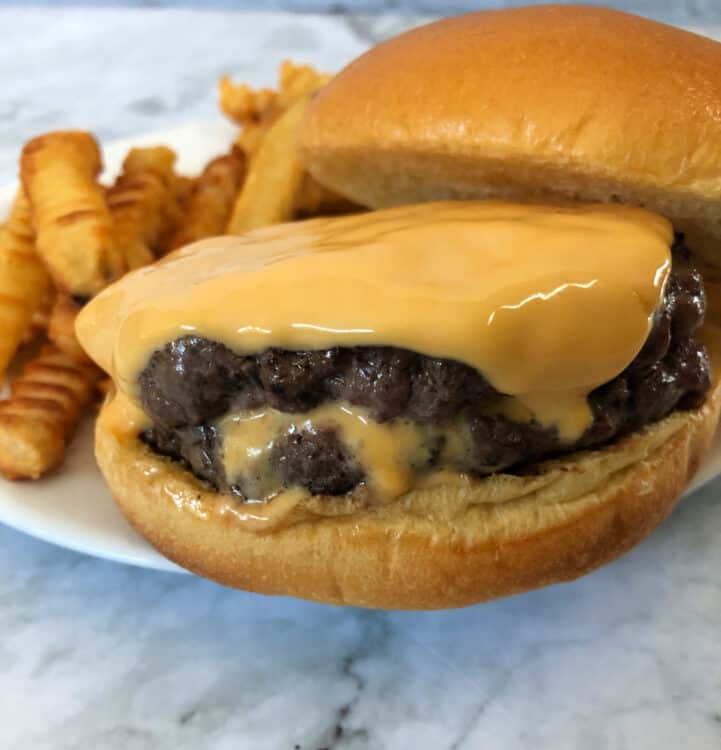 Juicy Lucy burger with extra cheese on top, showing stuffed cheese oozing from the middle