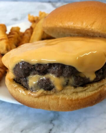 Juicy lucy stuffed burger with extra cheese on top and some cheese oozing from the burger