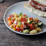 Easy pasta salad served on a plate with a brat in a bun