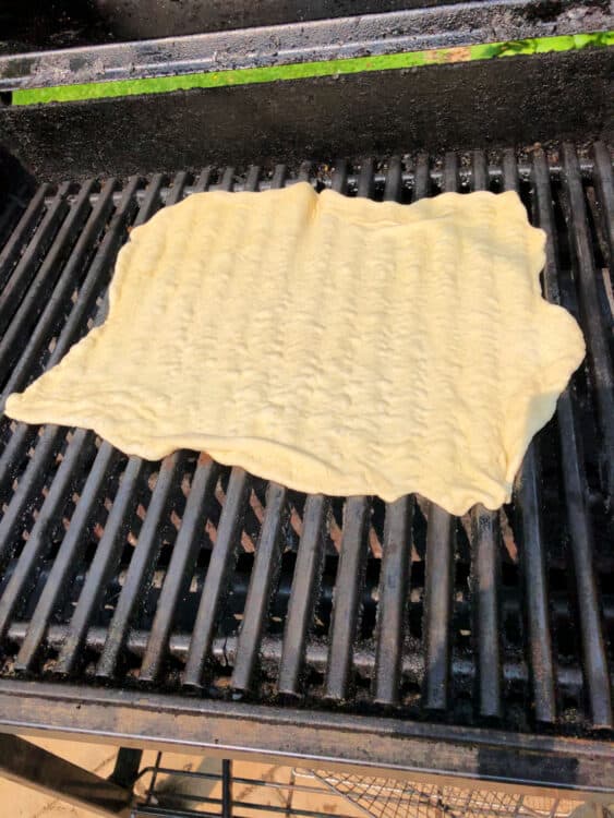raw pizza crust placed on BBQ grill grates