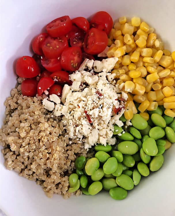 ingredients in a bowl: quinoa, tomato, corn, edamame, and feta cheese