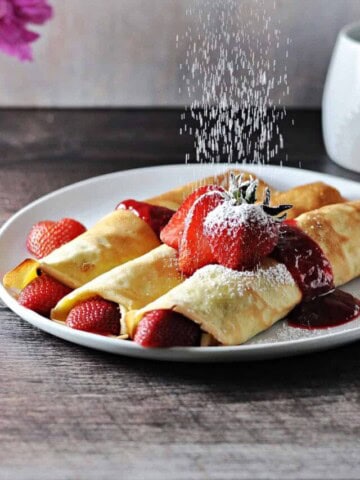 almond milk crepes with fruit being dusted with powdered sugar