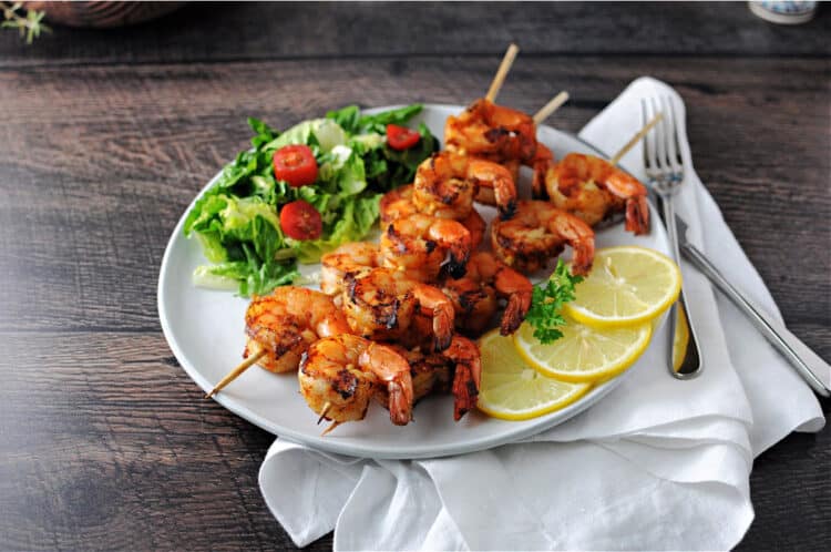 Cajun shrimp kabobs on a plate with a small green salad and lemon slices