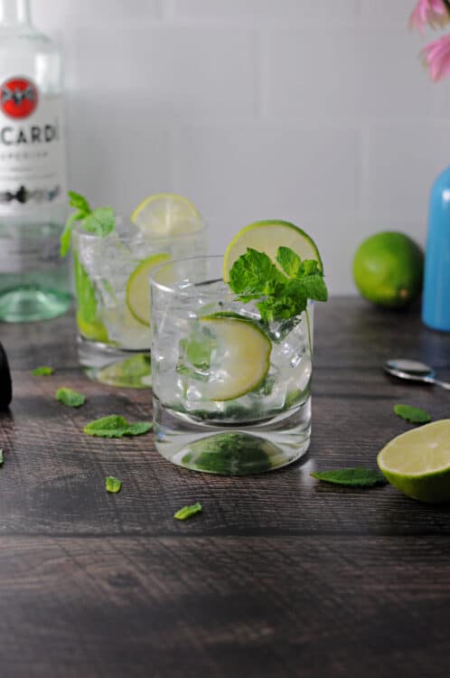 2 glasses of mojitos surrounded by mint leaves and lime