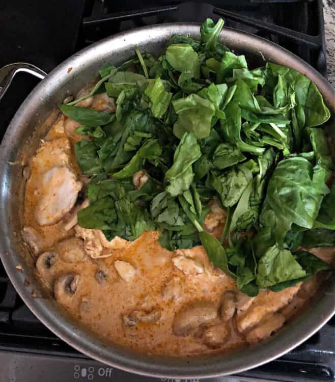 Sun dried tomato pesto chicken in a pan, adding spinach