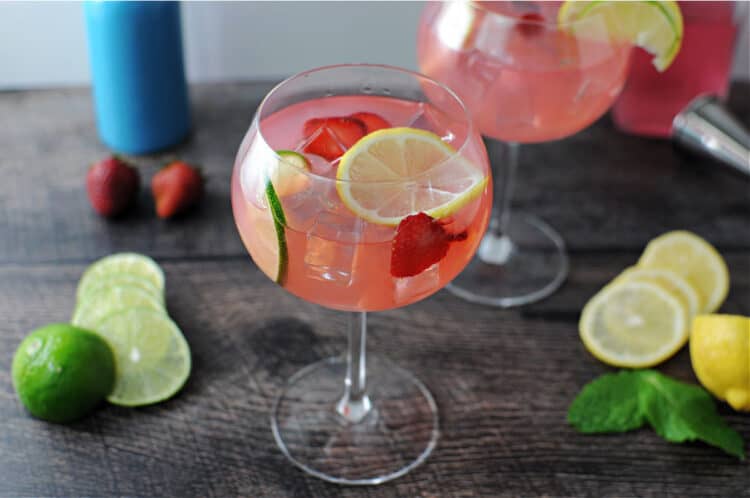 pink gin & lemonade drink in a wine glass garnished with lemon, lime and strawberry slices