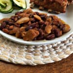 vegetarian baked beans on a white plate with a green b=vegetable and ribs behind