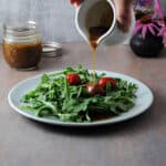 small pitcher pouring balsamic vinaigrette onto a plate of salad greens