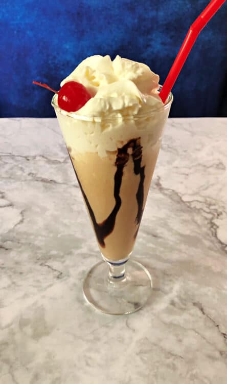 Kahlua mudslide ice cream drink in a tall glass topped with whipped cream and a cherry