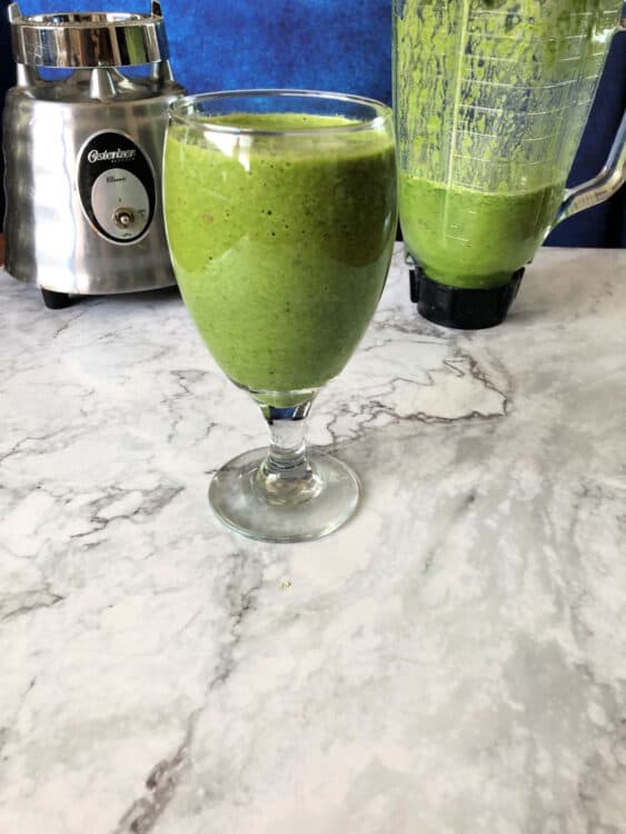 green smoothie in a glass with blender behind