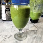 glass of green smoothie with blender behind