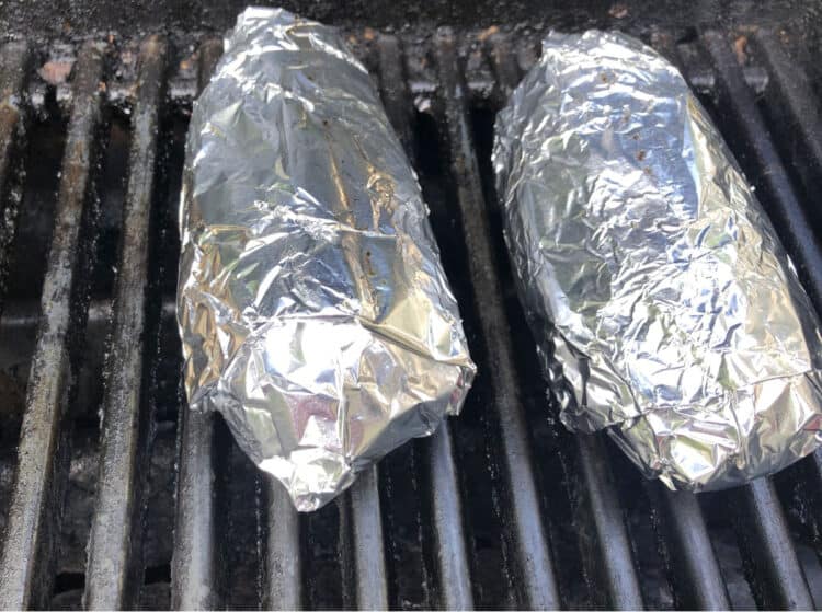 foil wrapped potatoes on black grill grates