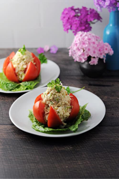 tuna stuffed tomato on a small plate, second serving behind it as well as flowers in a vase