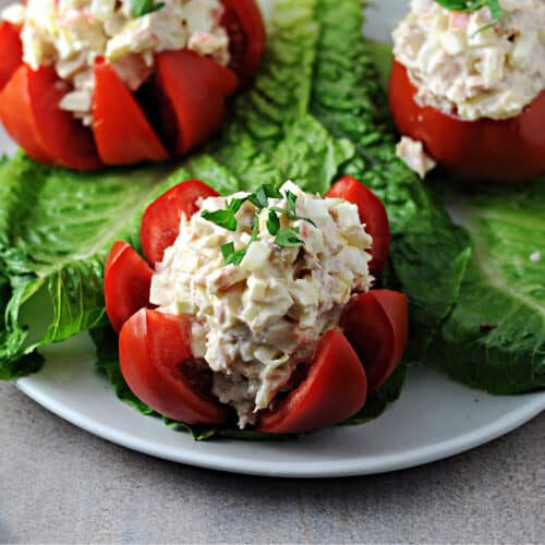tuna stuffed tomato on a lettuce covered plate with 2 others behind