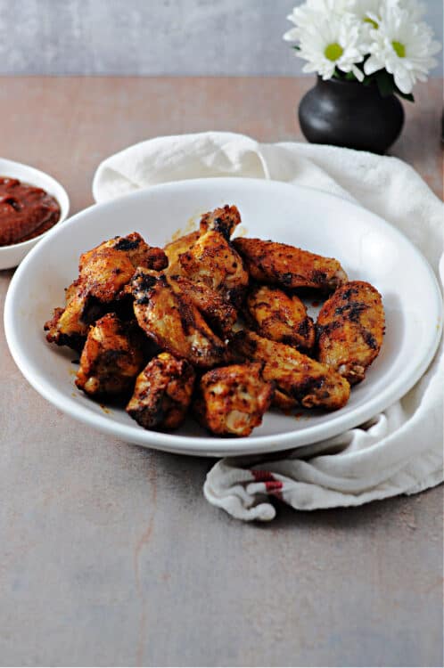 air fried wings in a serving bowl, small vase of flowers behind