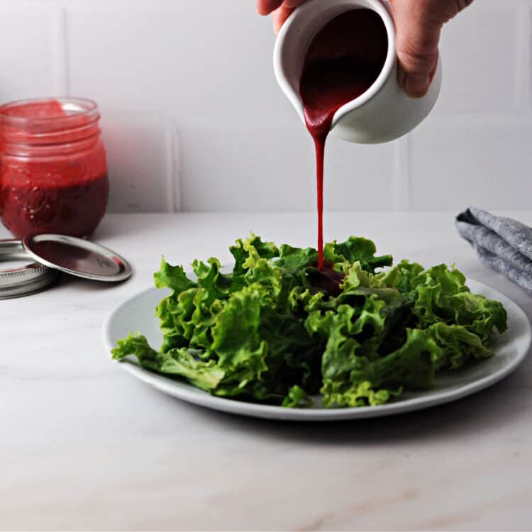 raspberry balsamic vinaigrette pouring from a small white pitcher onto some salad greens